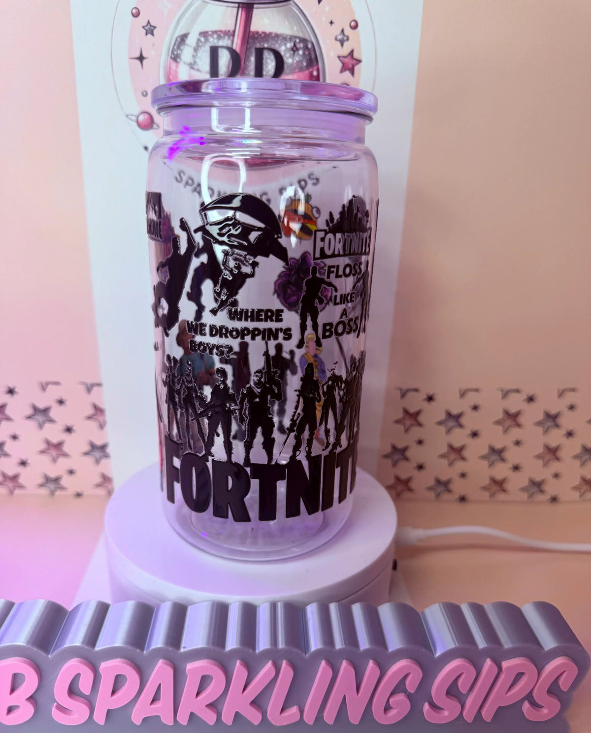 Fortnite-themed glitter tumbler with character silhouettes and 'Floss Like a Boss' text, displayed on a pink stand.