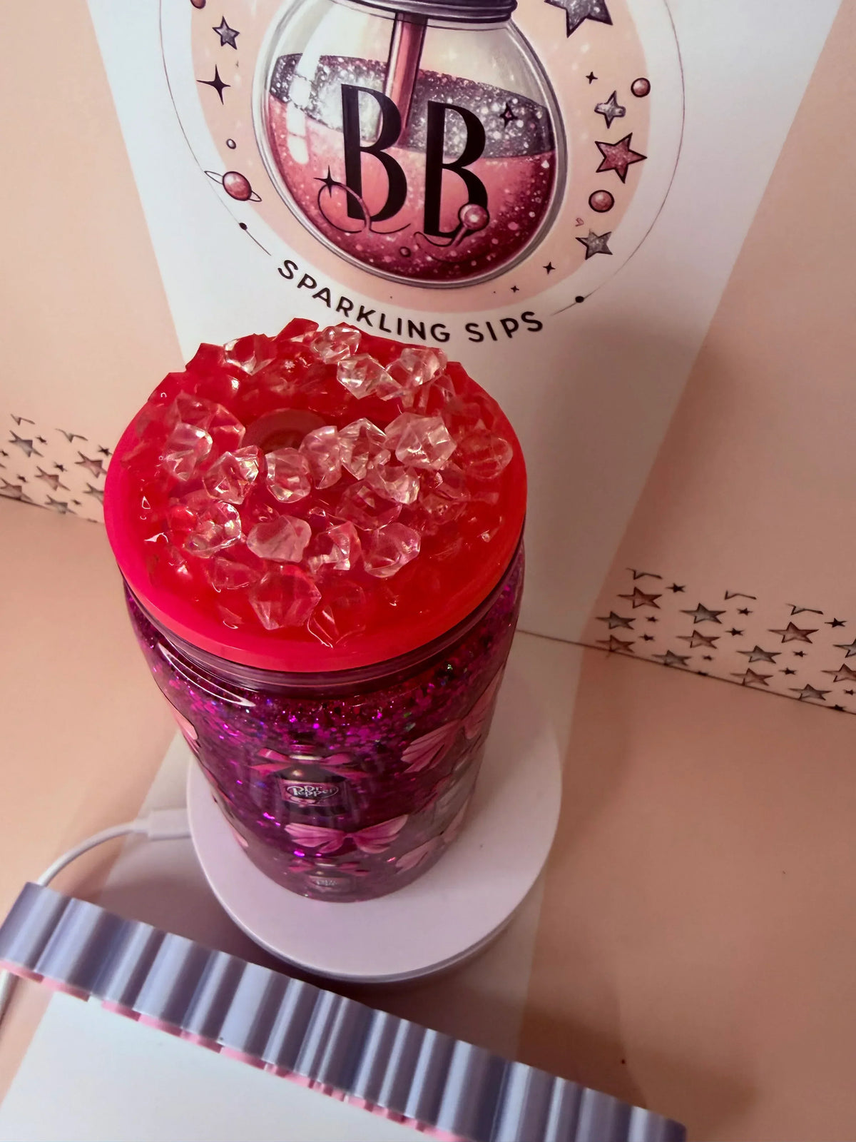 Pink glitter tumbler with red lid and ice cubes, featuring custom design and sparkling accents