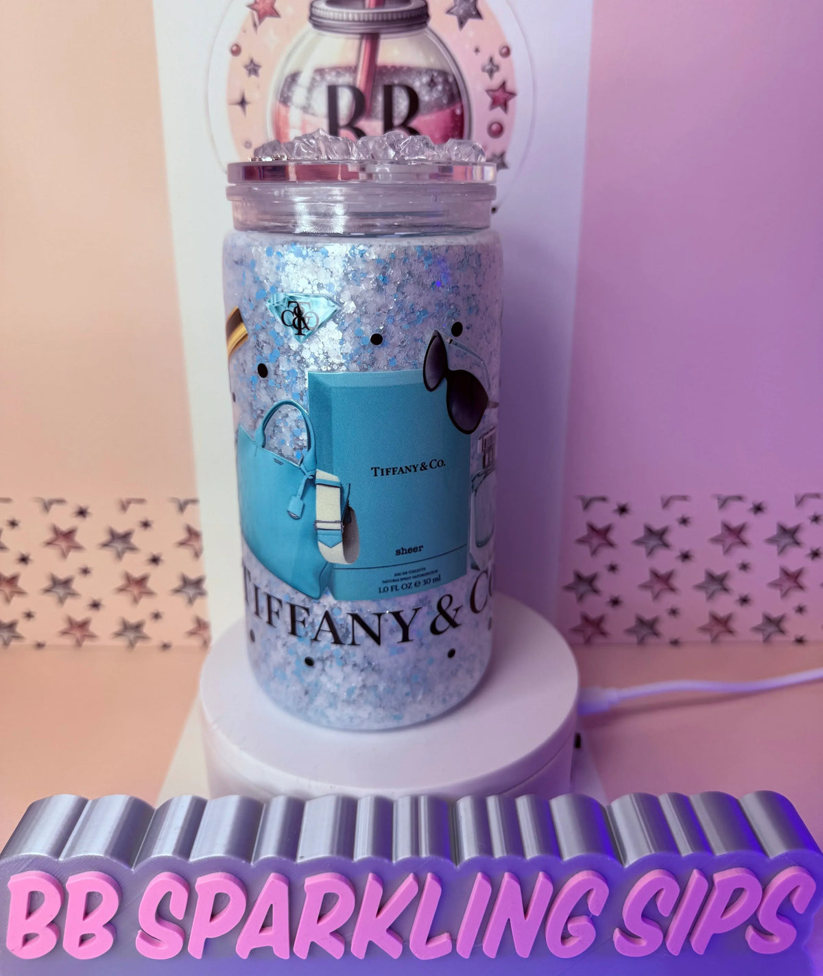 Glitter tumbler with Tiffany & Co. design, featuring blue bag and sunglasses, on a pink starry background.