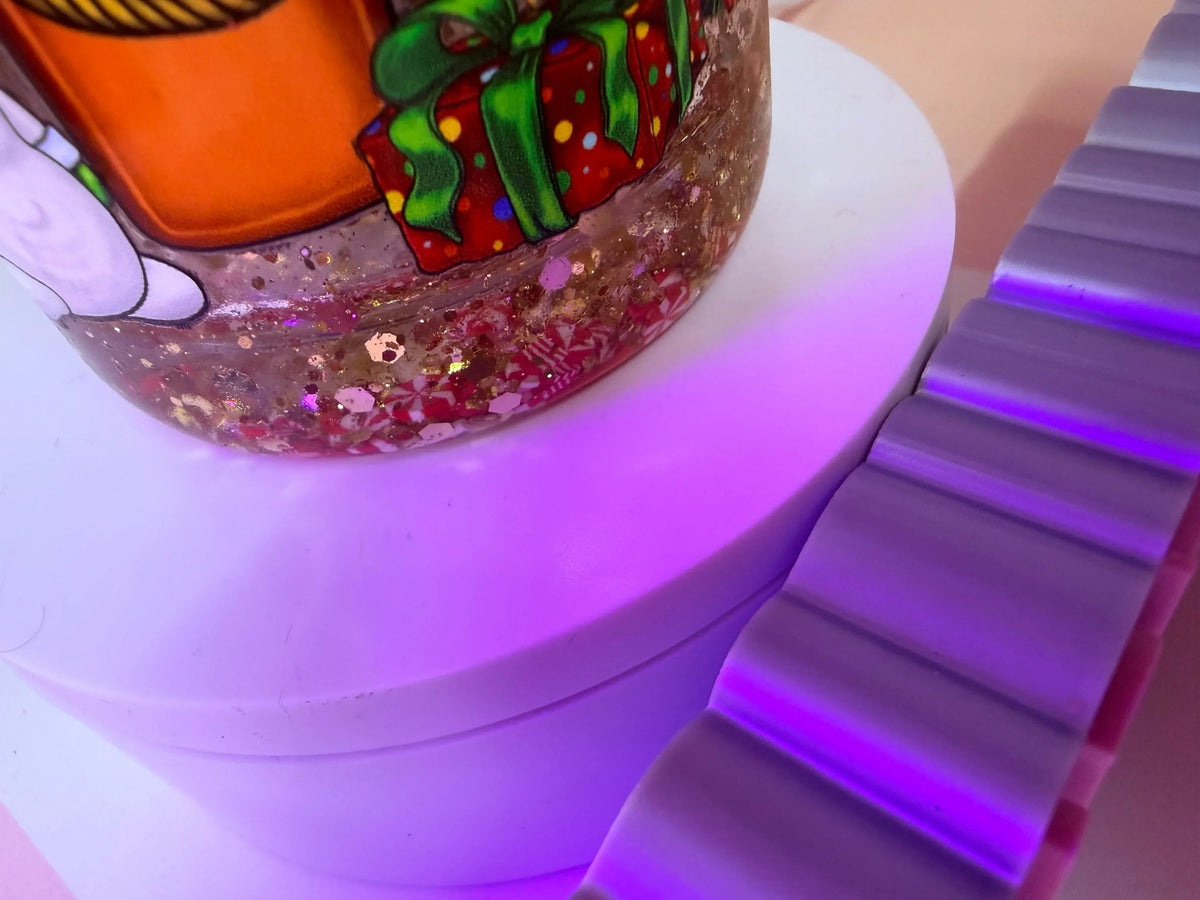 Glittery holiday-themed cup with gift design, glowing purple base, festive sparkle details